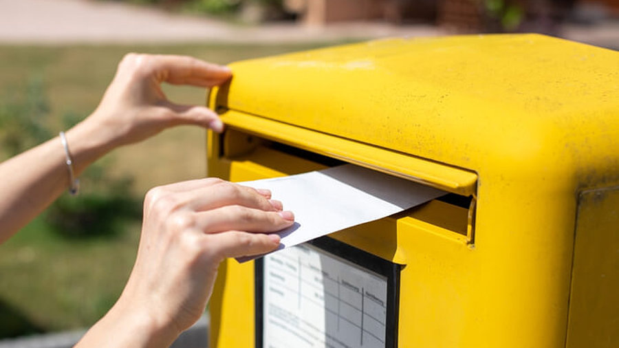 Person steckt Brief in Deutsche Post Briefkasten