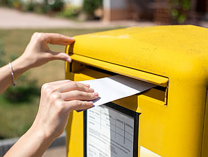 Person steckt Brief in Deutsche Post Briefkasten