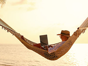 Person mit Laptop in der H&auml;ngematte am Strand