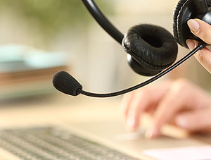 Person arbeitet von zu Hause aus am Notebook und hat ein Headset in der Hand