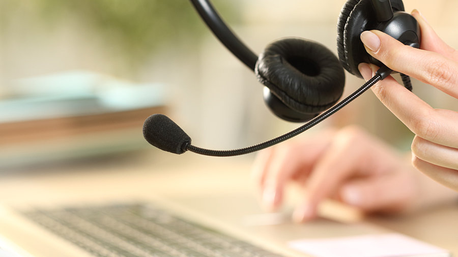 Person arbeitet von zu Hause aus am Notebook und hat ein Headset in der Hand