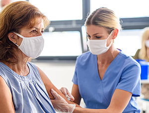 Frau mit Maske wird von &Auml;rztin geimpft