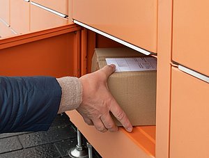 Person nimmt Paket aus Paketschlie&szlig;fach