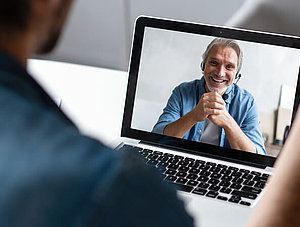 Mann in Videokonferenz vor Laptop