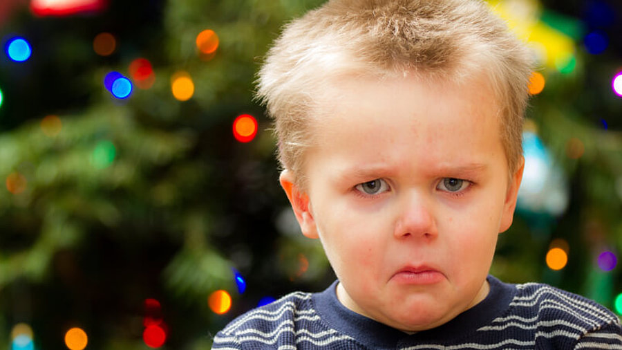 missmutiger Junge vor Weihnachtsbaum