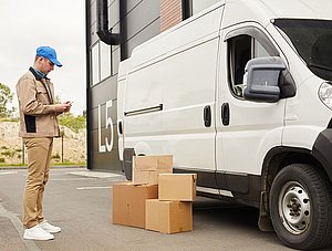 Paketbote neben Lieferauto und Paketen