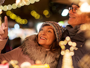 Ehepaar mittleren Alters steht vor Verkaufsstand auf dem Weihnachtsmarkt