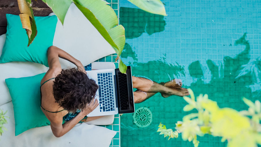 Frau sitzt mit Laptop am Pool