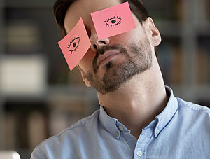 Person hat Post-its mit aufgemalten Augen aufgeklebt sitzt vor Laptop