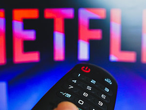 Netflix-Logo und Hand an TV-Fernbedienung