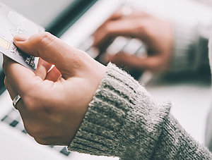 Frau sitzt mit Kreditkarte in der Hand vor PC und gibt Daten ein.