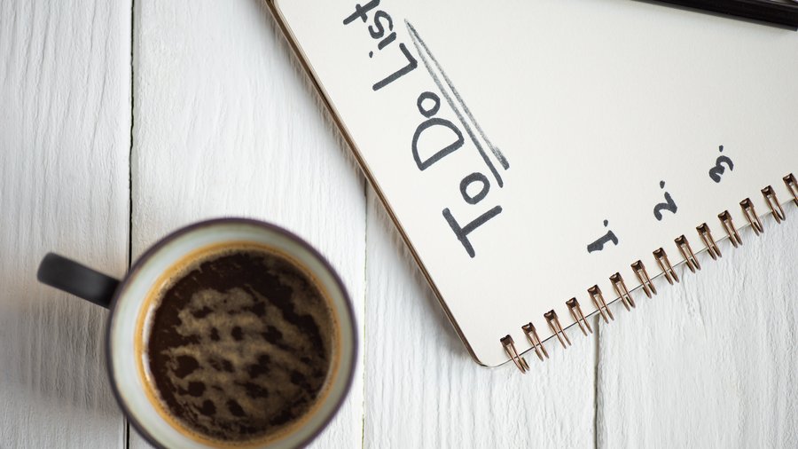  Das Bild zeigt einen Notizblock mit der Aufschrift "To Do" und eine Tasse Kaffee auf einem weißen Holztisch. Der Notizblock ist aufgeschlagen und ein Stift liegt daneben.