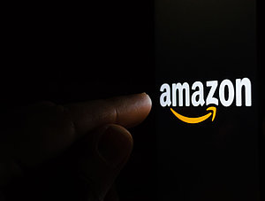 Finger zeigt auf Amazon-Logo vor schwarzem Hintergrund