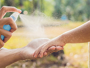 Person spr&uuml;ht Kind mit Spray ein