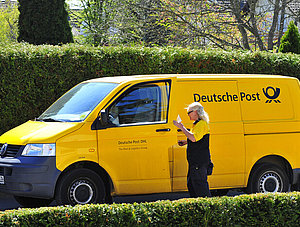 Postbotin an Zustellfahrzeug der Deutschen Post