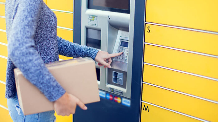 Frau mit Paket an Paketstation