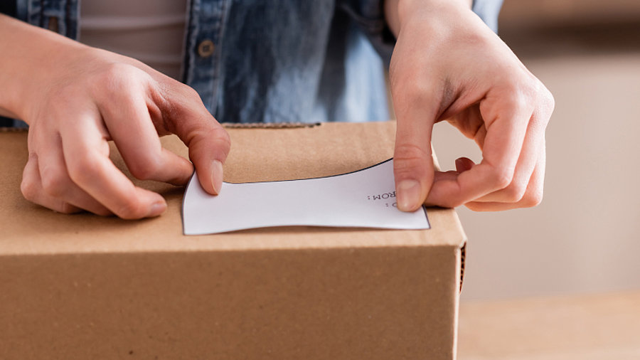 Person klebt Etikett auf Paket