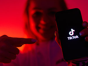 Frau zeigt auf Smartphone mit TikTok