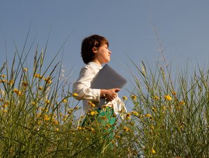 Junge Frau geht mit Laptop unterm Arm durch Blumenfeld