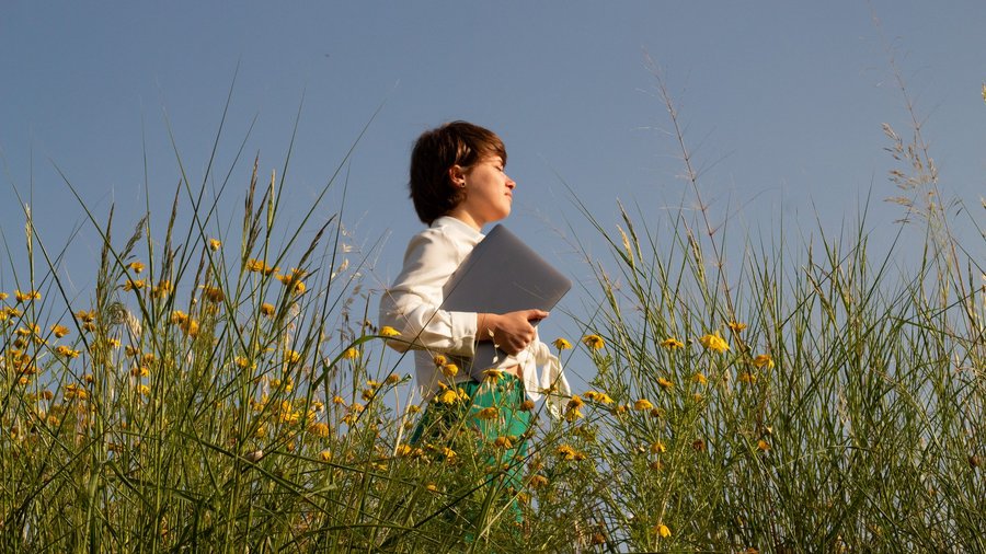 Junge Frau geht mit Laptop unterm Arm durch Blumenfeld