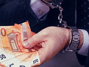 Mann in Handschellen h&auml;lt Bargeld