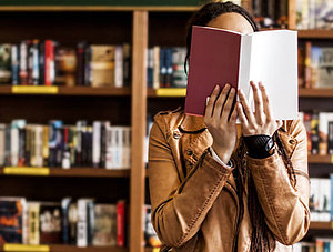 Frau in Buchladen h&auml;lt sich Buch vor das Gesicht