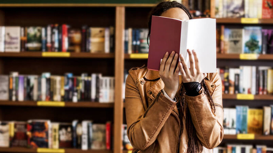 Frau in Buchladen h&auml;lt sich Buch vor das Gesicht