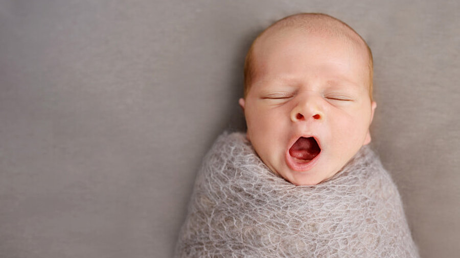 Gähnendes Baby eingewickelt in eine Decke