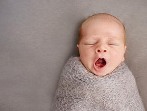 Gähnendes Baby eingewickelt in eine Decke