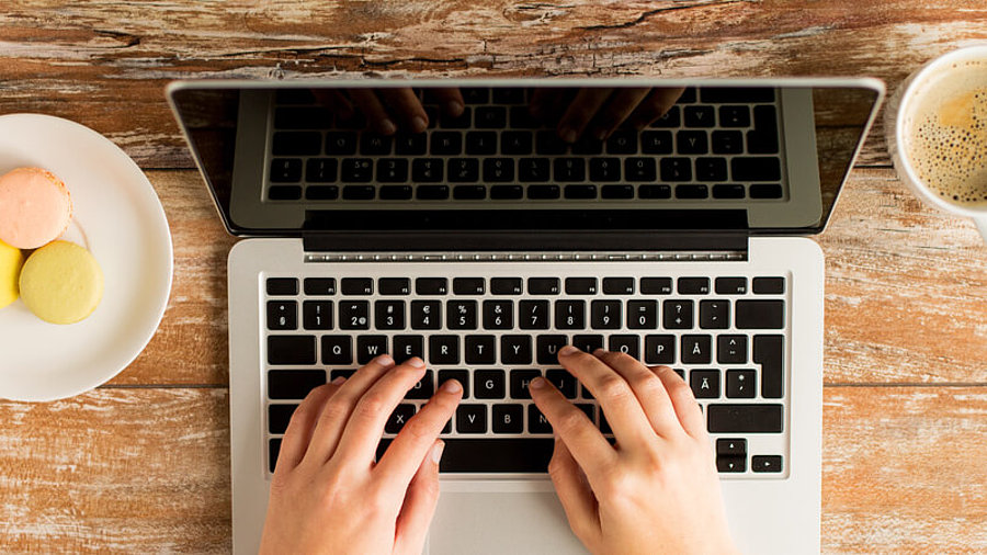 Person vor Laptop mit Keksen und Kaffee