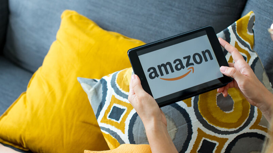 Frau mit Amazon-Tablet auf farbenfrohem Sofa