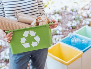 Frau hält Recycling-Behälter mit Pappe in den Händen 