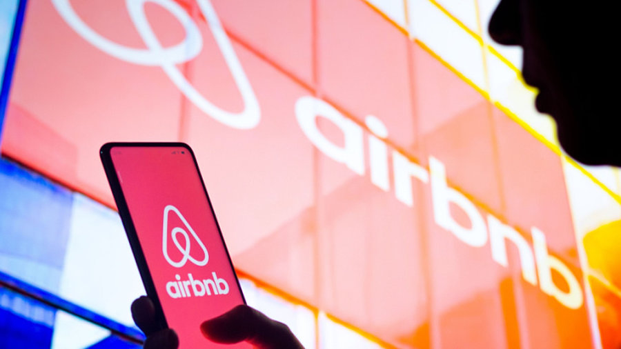 Airbnb-Logo an Geb&auml;ude und auf Smartphone