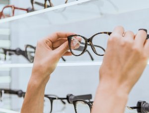 Person nimmt Brille aus Auslage beim Optiker