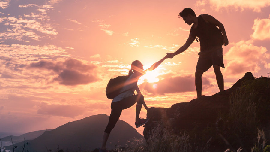 Menschen, die einander helfen, wandern bei Sonnenaufgang einen Berg hoch