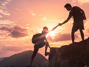 Menschen, die einander helfen, wandern bei Sonnenaufgang einen Berg hoch