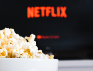 Schale Popcorn, i Hintergrund ein Bildschirm, auf dem verschwommen das Logo von Netflix zu sehen ist