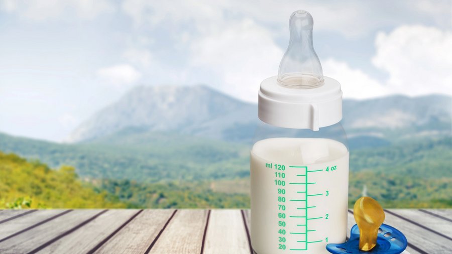 Flasche mit Babymilch steht auf Holztisch in bergigem Land