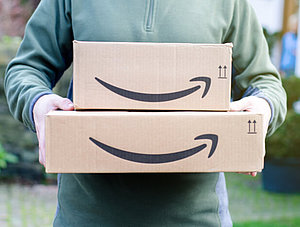 Mann trägt zwei Amazon-Pakete