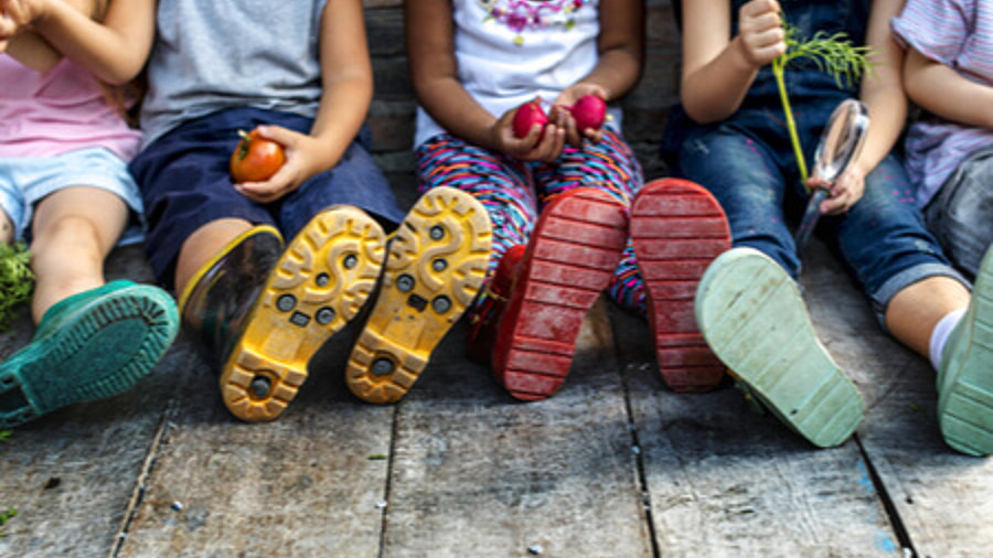 Vorschule für ärmere Kinder: Kids sitzen auf dem Boden und halten Gemüse in den Händen