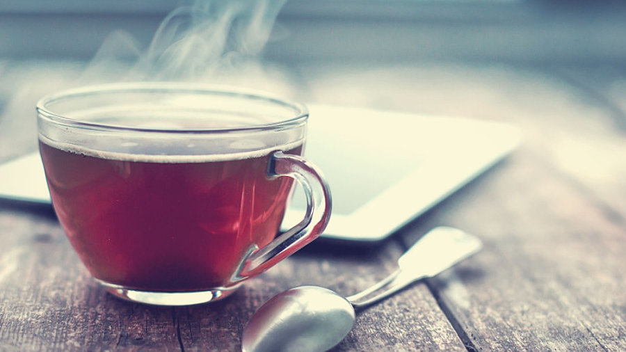 Tasse mit schwarzem Tee auf Holztisch