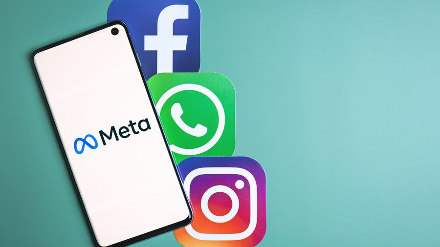  Das Bild zeigt ein Smartphone mit dem Meta-Logo auf dem Bildschirm. Neben dem Smartphone befinden sich die Logos von Facebook, WhatsApp und Instagram auf einem grünen Hintergrund.