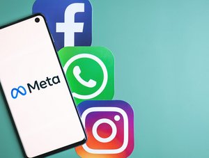  Das Bild zeigt ein Smartphone mit dem Meta-Logo auf dem Bildschirm. Neben dem Smartphone befinden sich die Logos von Facebook, WhatsApp und Instagram auf einem grünen Hintergrund.