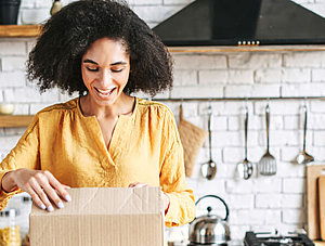 Frau packt fr&ouml;hlich ein Paket aus, das online bestellt wurde