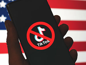 Durchgestrichenes TikTok-Logo auf Mobiltelefon vor US-Flagge