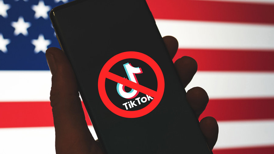 Durchgestrichenes TikTok-Logo auf Mobiltelefon vor US-Flagge