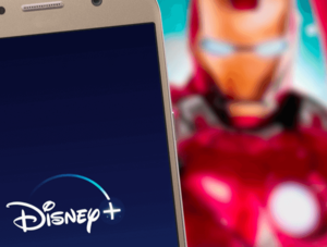 Disney+-App auf einem Smartphone. Streaming-Dienst auf TV dahinter.