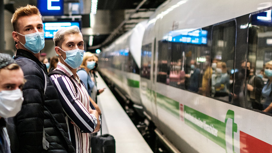 Menschen mit Maske warten auf Fernverkehrszug