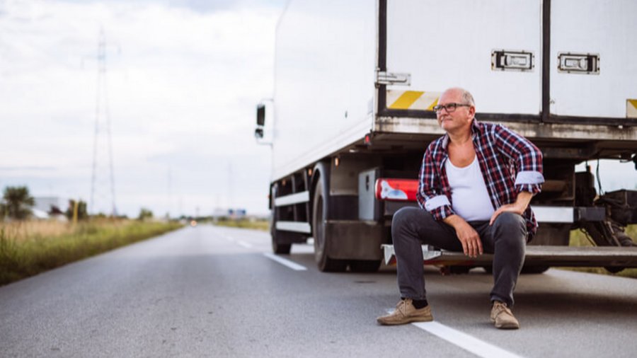 Älterer Lkw Fahrer sitzt neben seinem LKW