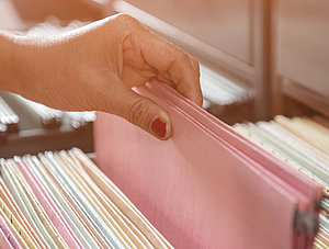 Hand greift im Aktenschrank nach Akte